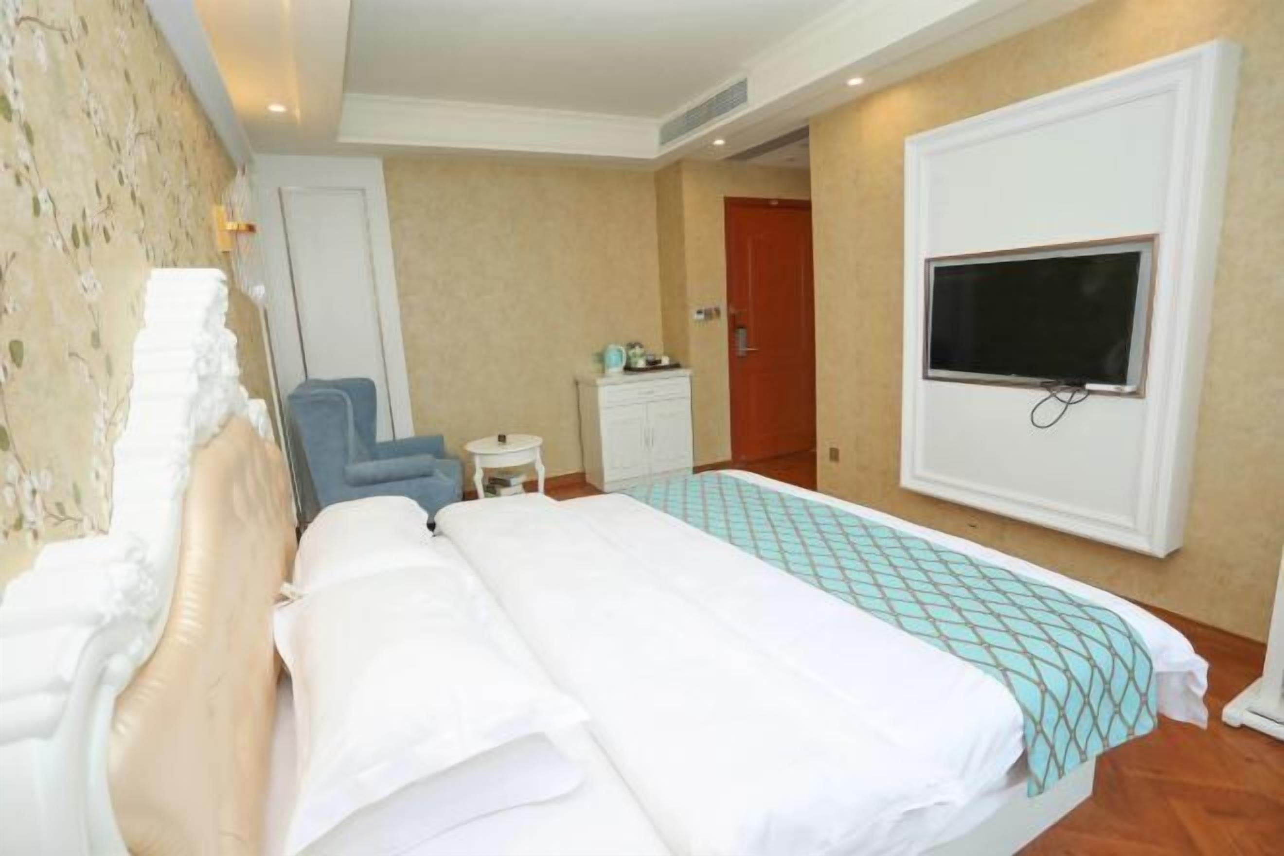 A hotel room with a bed, a TV mounted on the wall, a small table, and a chair.
