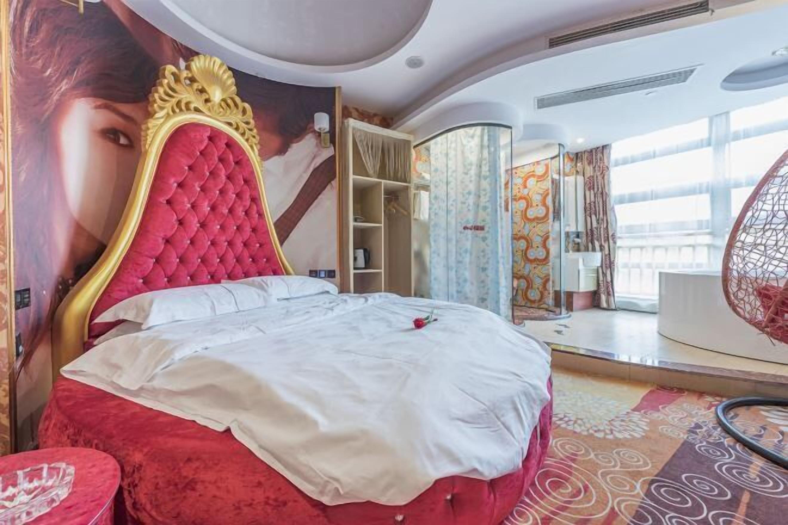 Une chambre avec un lit rouge, un grand miroir et une vue sur l’extérieur.
