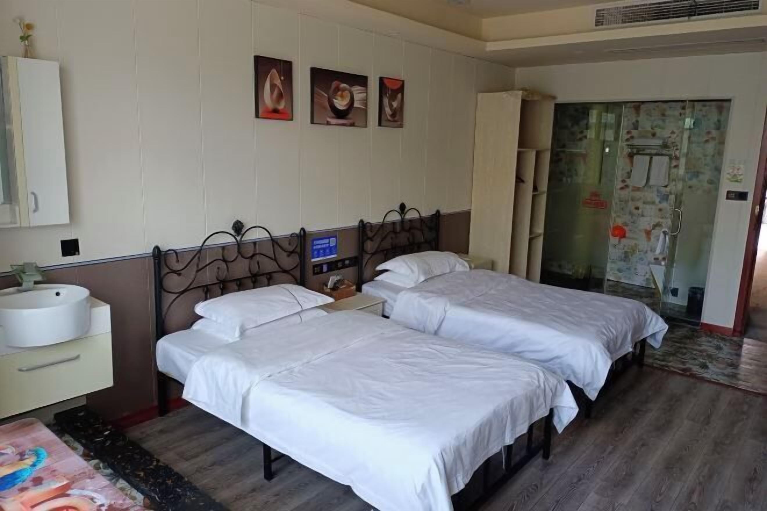 A hotel room with two single beds, a bedside table with a lamp, a large window, and a bathroom visible through a glass door.