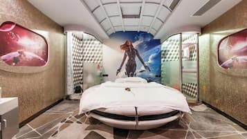 A room with a bed, a mirror, and a wall with a space-themed mural.