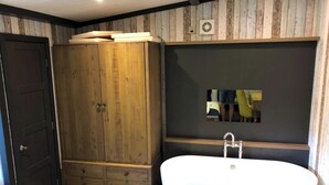 A bathroom with a wooden wardrobe, a freestanding bathtub, and a mirror on the wall. - Pet Friendly Lodge - Sleeps 6 (Fordingbridge)