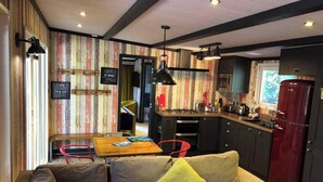 A cozy living room with a sofa and a dining table, a kitchen with modern appliances, and a striped wall design. - Pet Friendly Lodge - Sleeps 6 (Fordingbridge)