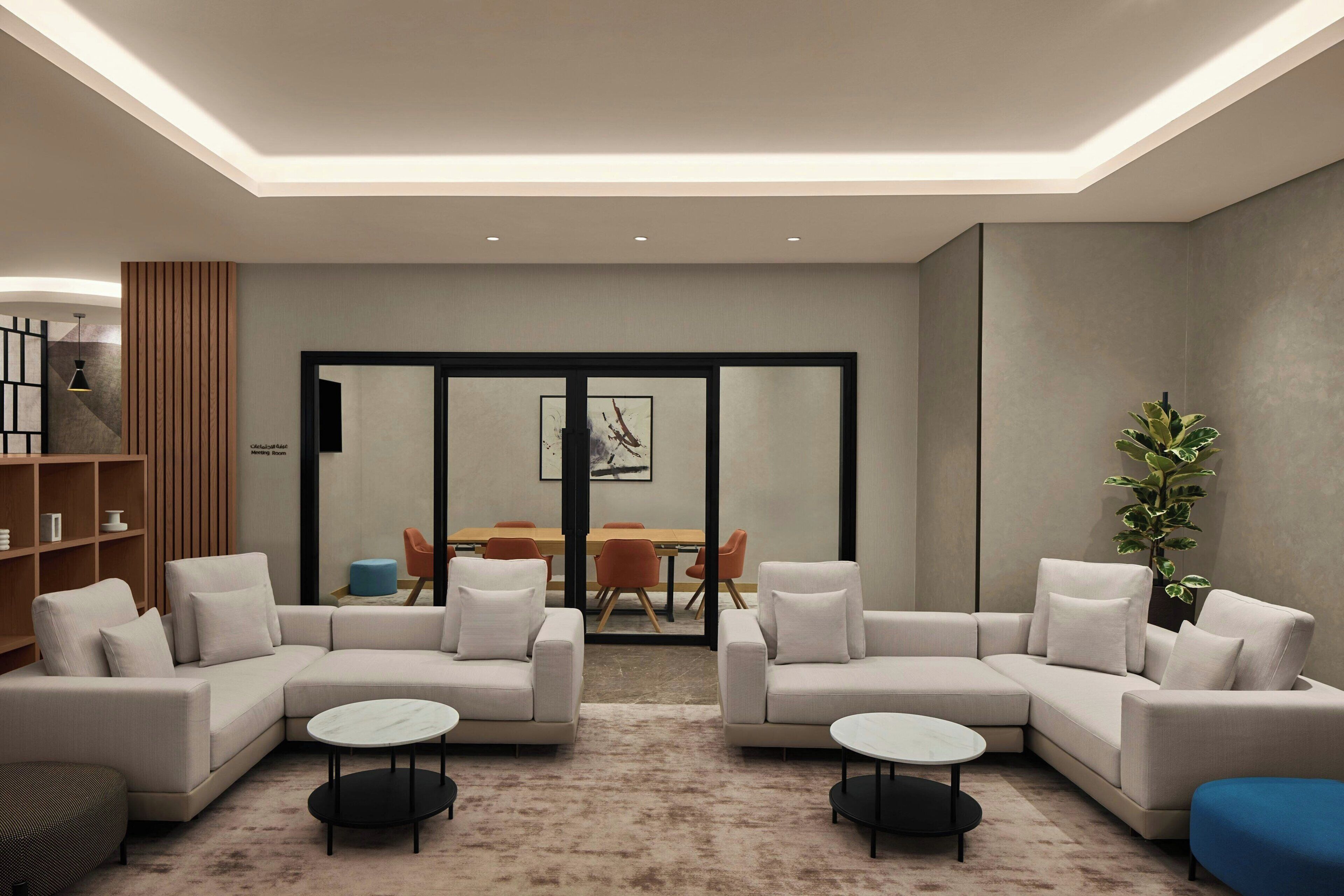 A modern living room with a sectional sofa, two round coffee tables, a bookshelf, and a dining area with orange chairs and a wooden table.