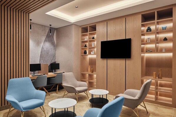 A modern lounge area with a flat-screen TV, wooden shelving, and seating. - Courtyard By Marriott Makkah (Makkah)