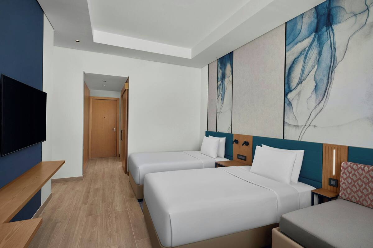 Habitación de hotel con dos camas, un televisor, un banco de madera y arte abstracto en la pared.