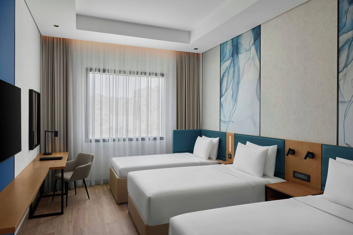 Habitación de hotel con dos camas, un escritorio, una silla, un televisor y un cuadro abstracto grande en la pared.
