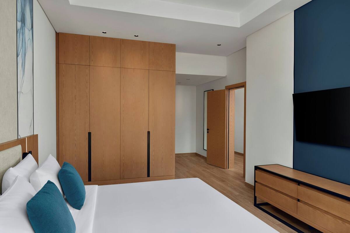 Habitación de hotel moderna con una cama grande, armario de madera, televisor de pantalla plana y diseño minimalista.