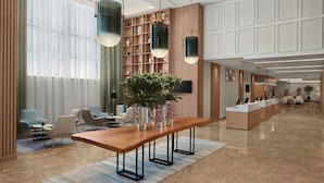 En rummelig lobby med en lang træreception, moderne stole og et stort vindue med lette gardiner.