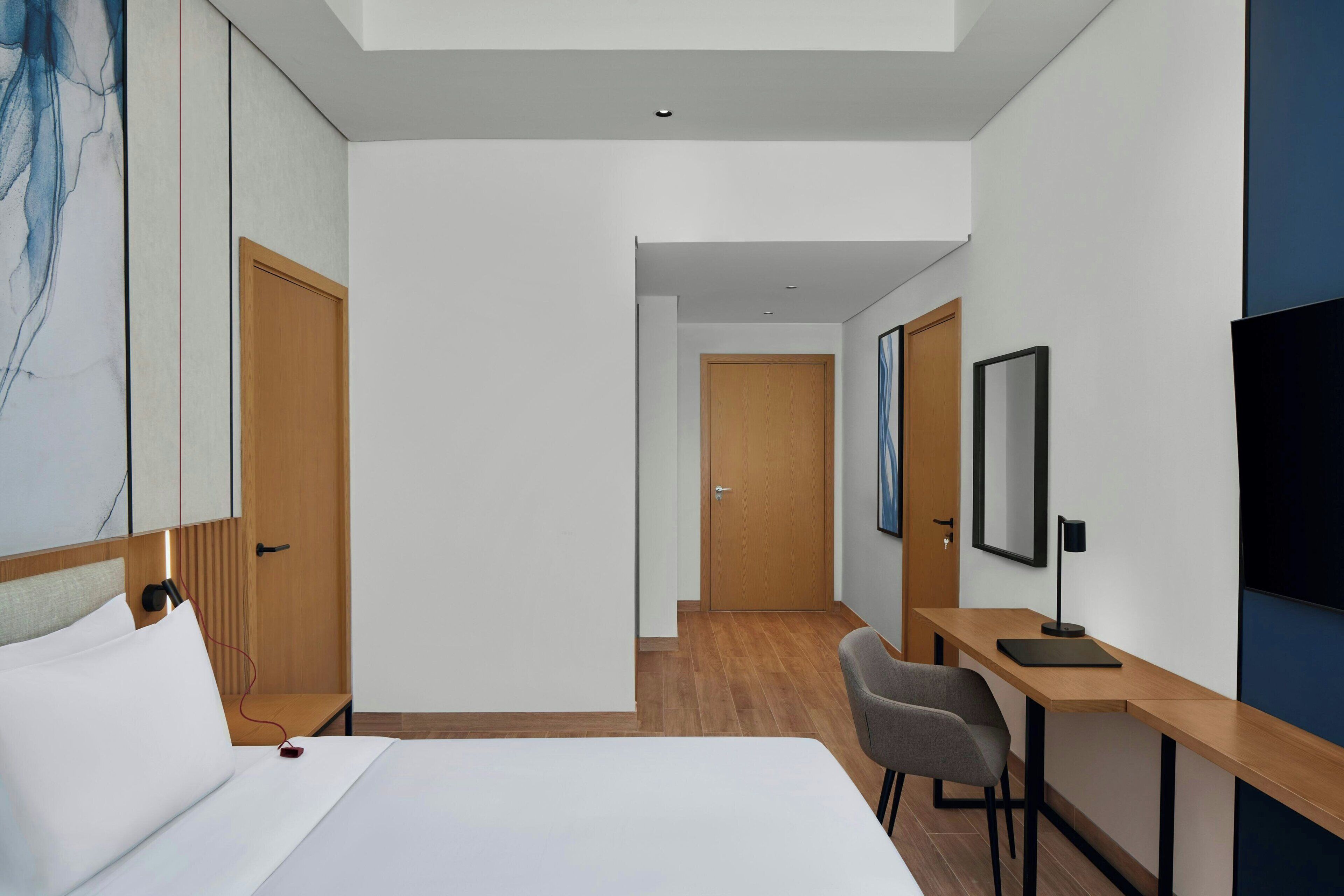 A hotel room with a bed, a desk, a chair, and a TV.
