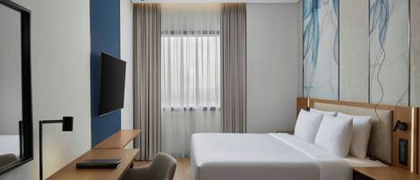 A modern hotel room with a bed, a desk, a chair, a TV, and a large abstract painting on the wall.