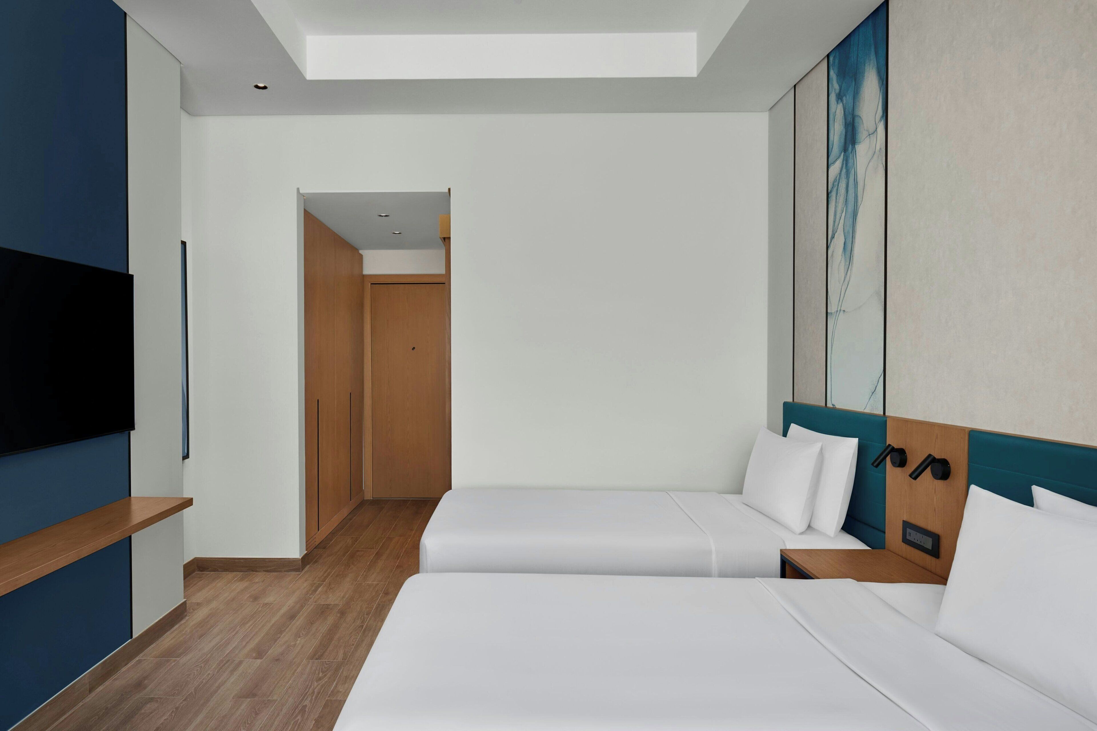 A modern hotel room with two beds, a TV, and a painting on the wall.