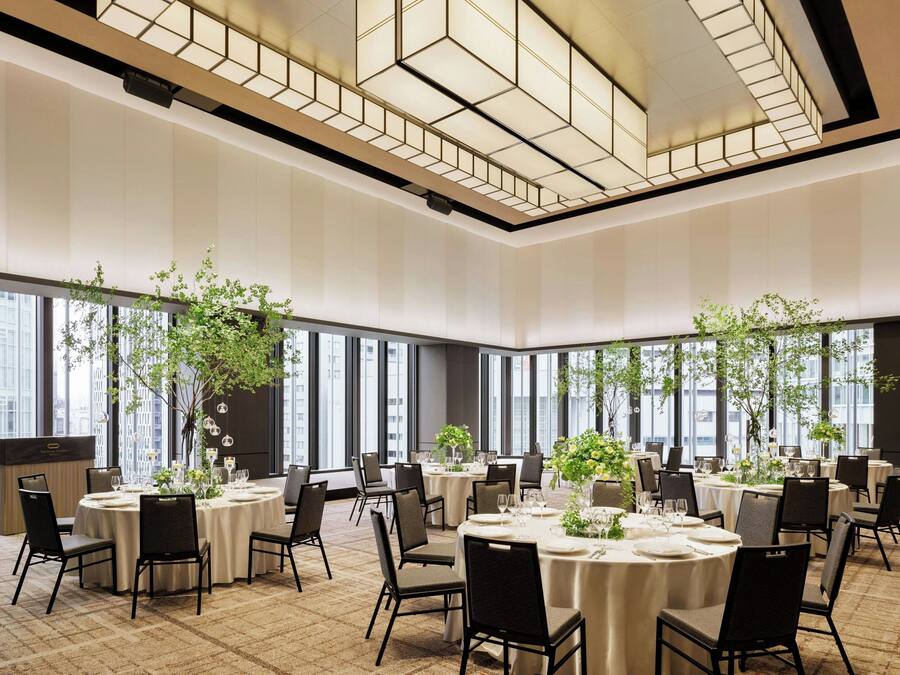 A spacious conference room with round tables, black chairs, and large windows offering city views.