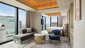A modern hotel room with a large window, a sofa, a round gold coffee table, a blue armchair, and a bed. - THE OSAKA STATION HOTEL, Autograph Collection (Osaka)