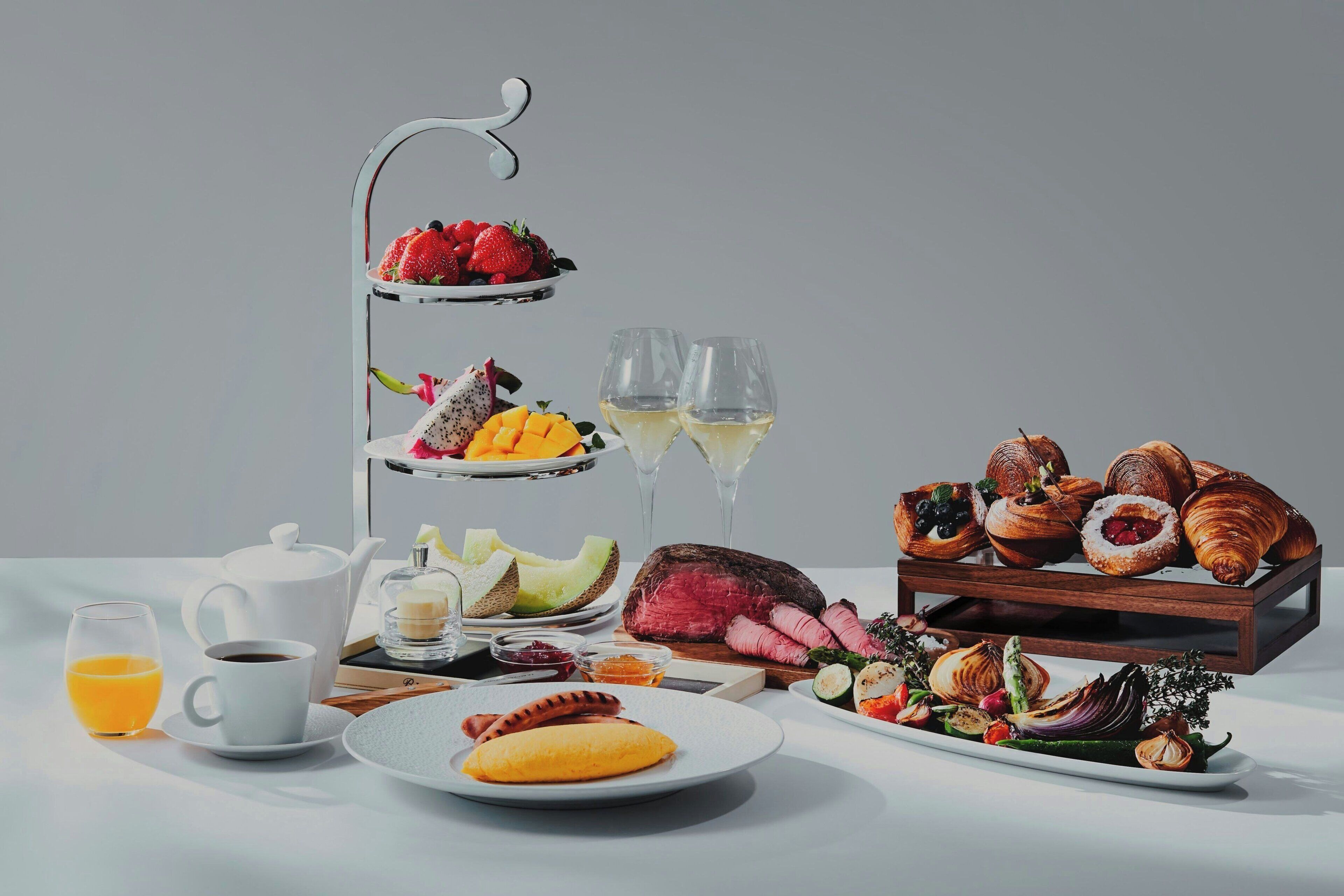 A three-tiered fruit and pastry stand with assorted fruits, pastries, and a bottle of wine.