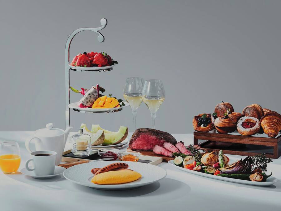 A three-tiered fruit and pastry stand with assorted fruits, pastries, and a bottle of wine.