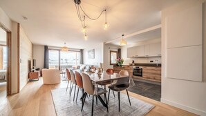 A modern kitchen with wooden cabinets, a dining area with a large table and chairs, and a view of the city through large windows.