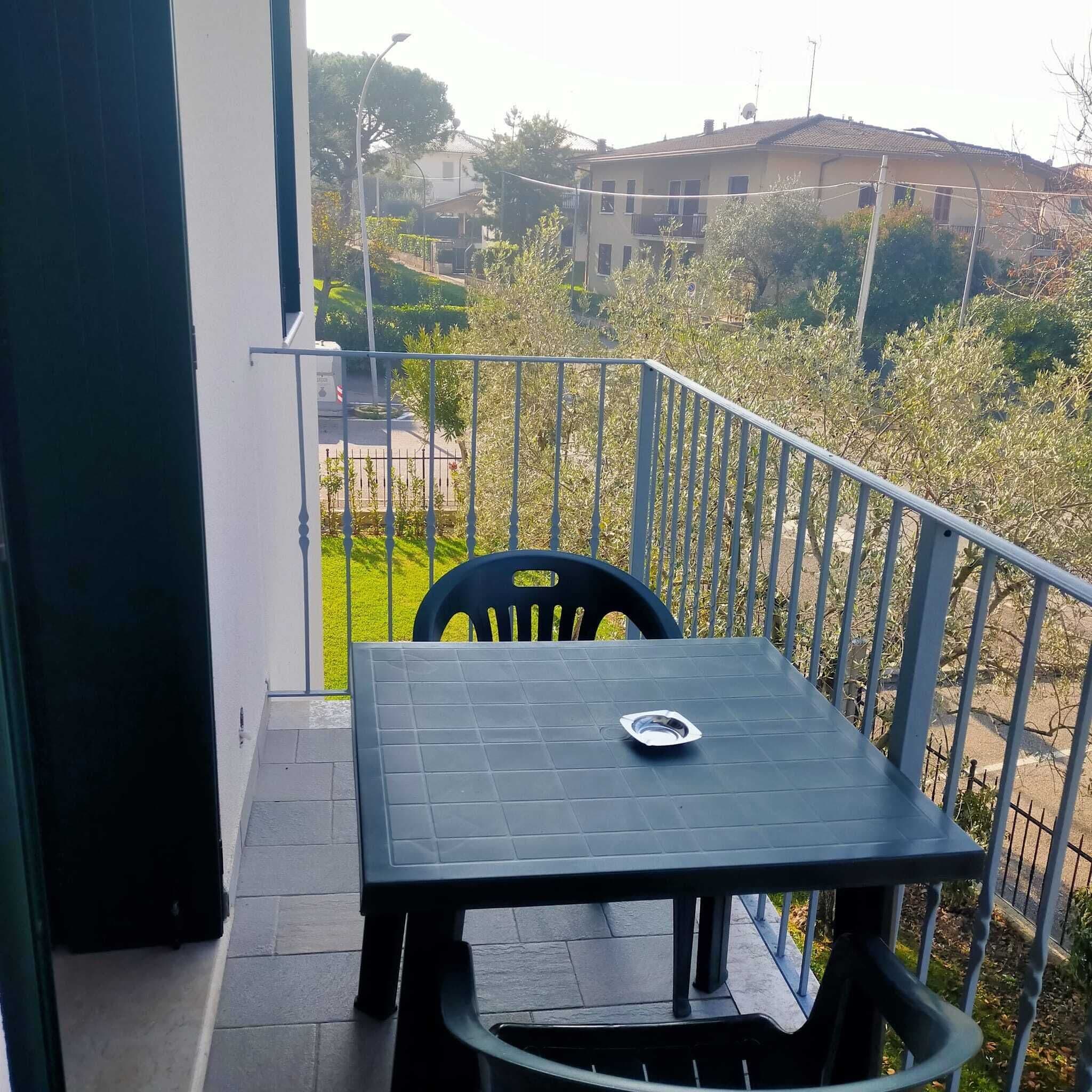 A balcony with a table and chairs, overlooking a garden and buildings.