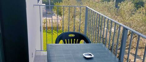 A balcony with a table and chairs, overlooking a garden and buildings.