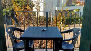 Un balcone con tavolo e due sedie, affaccia su una zona residenziale con alberi e palazzi.