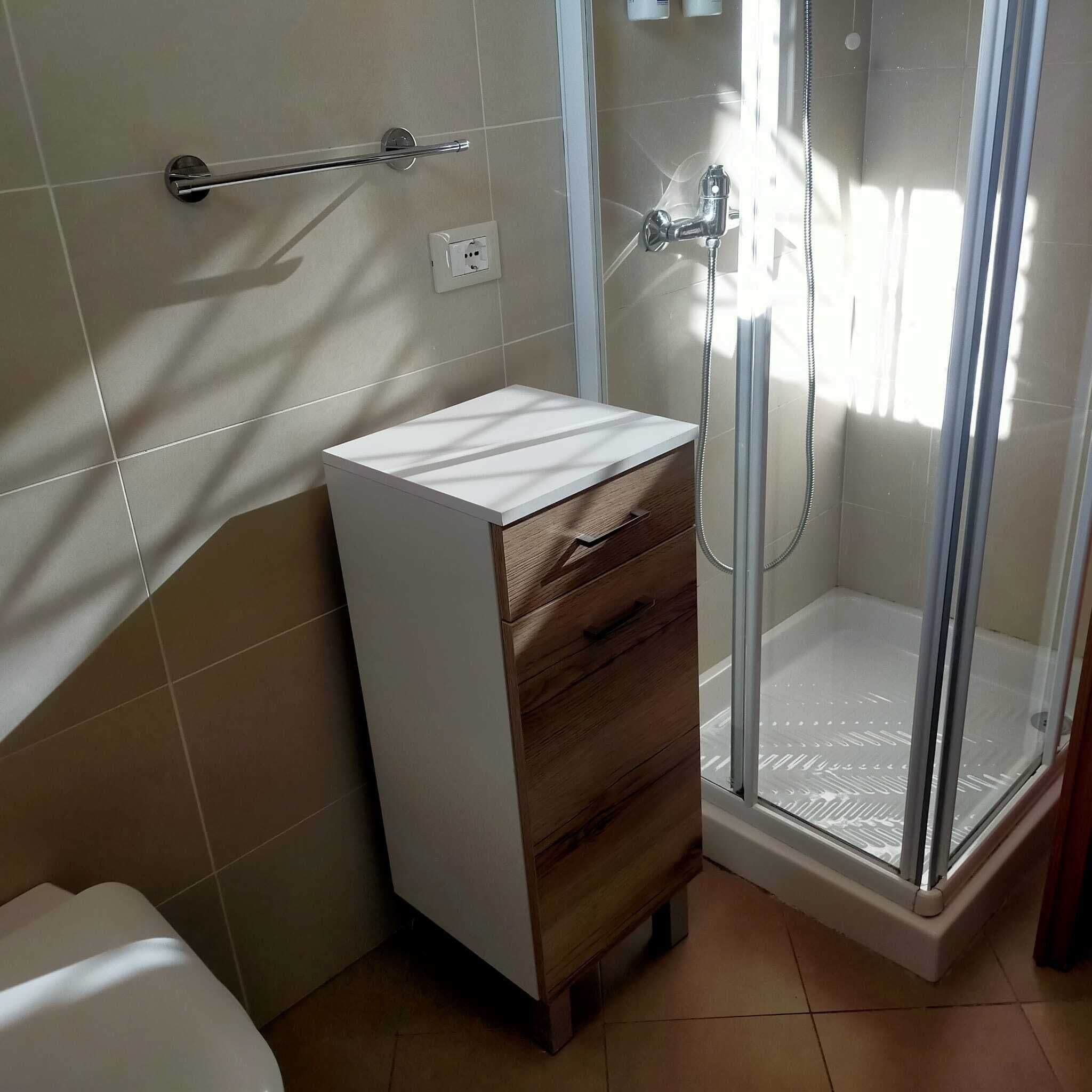 Un baño con ducha, tocador con cajones y perchero para toallas.