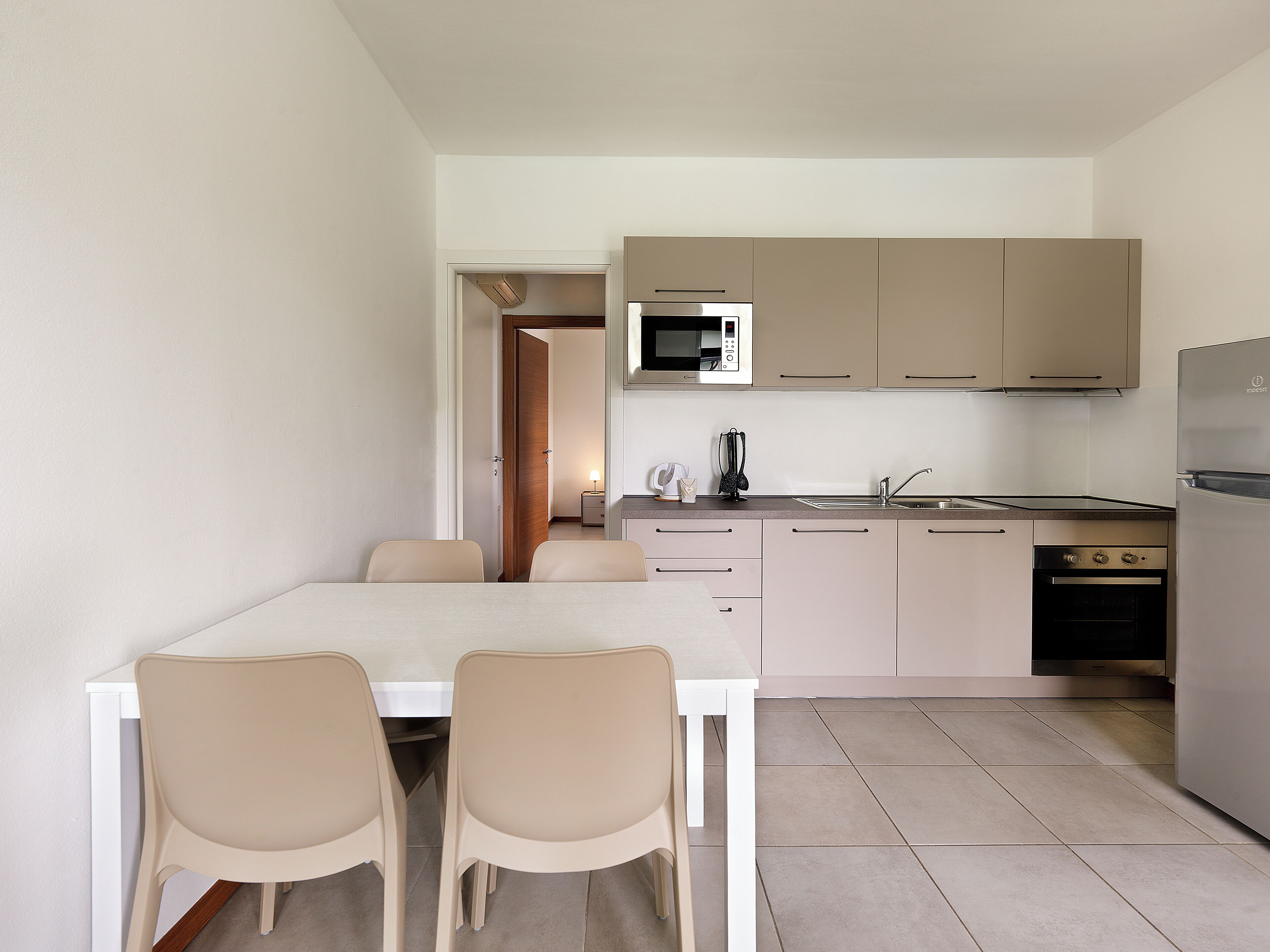 Een moderne keuken met een eetgedeelte, met een tafel en stoelen, een magnetron, een spoelbak en een koelkast.