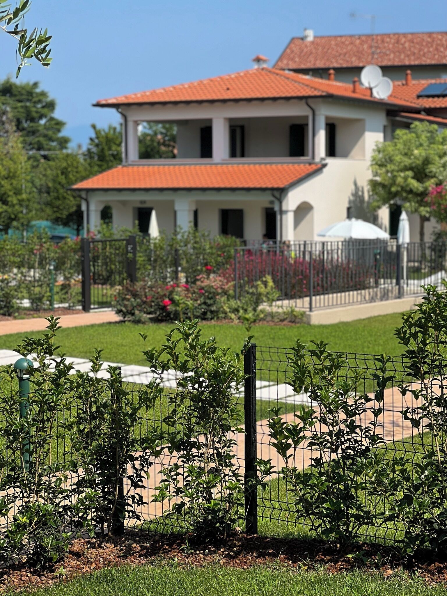 A two-story building with a red-tiled roof, surrounded by a garden with a fence.