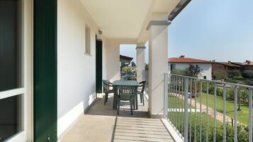 Ein Balkon mit Tisch und Stühlen, eine grüne Tür und Blick auf einen Garten und Gebäude.