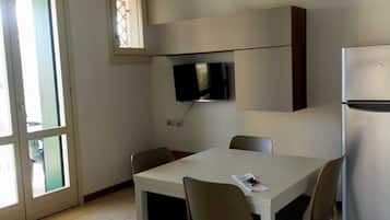 Una cocina pequeña y moderna con una mesa y sillas blancas, televisor integrado y refrigerador.