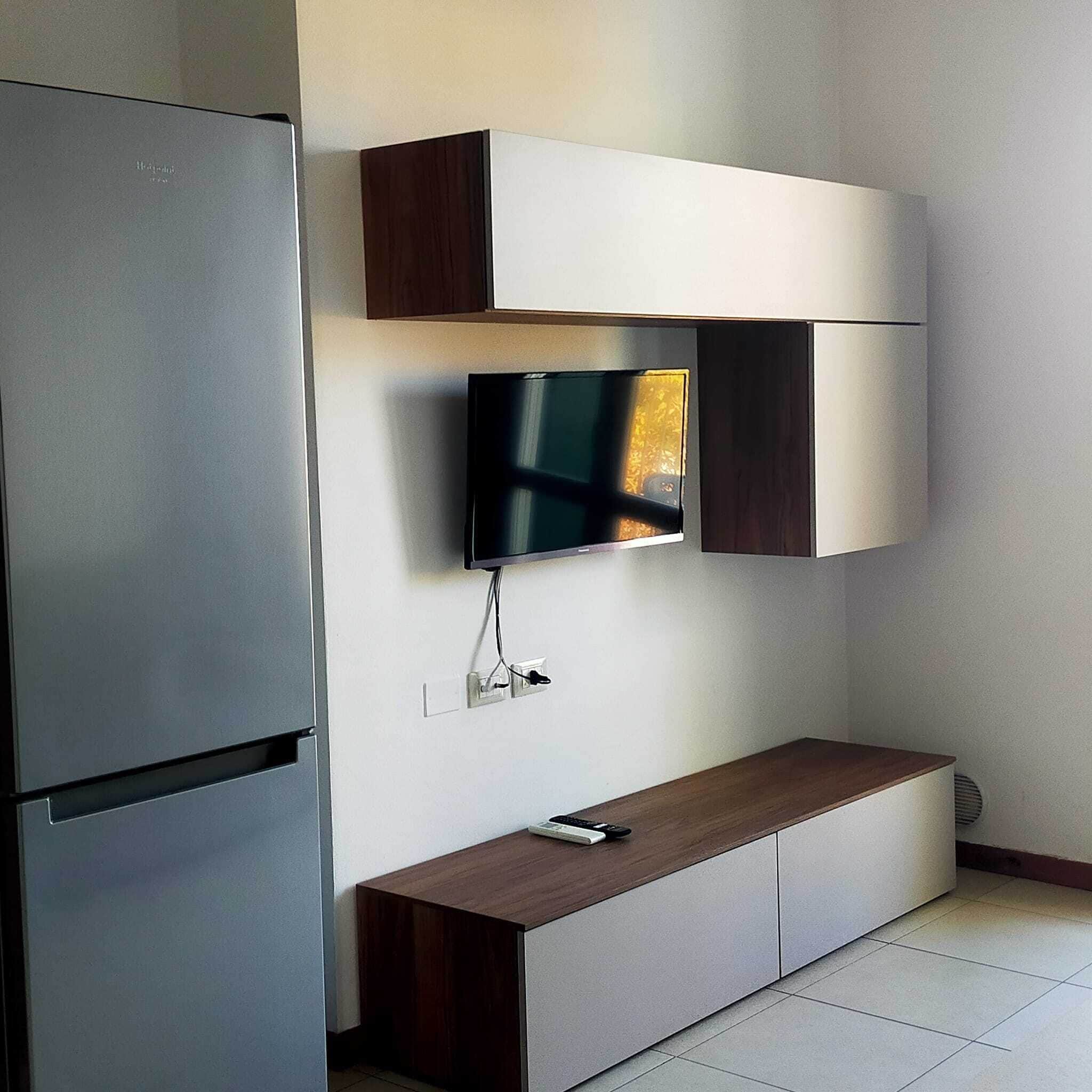 Una cocina moderna con refrigerador integrado, un televisor de pantalla plana montado en un mueble de madera y una pequeña mesa de madera.