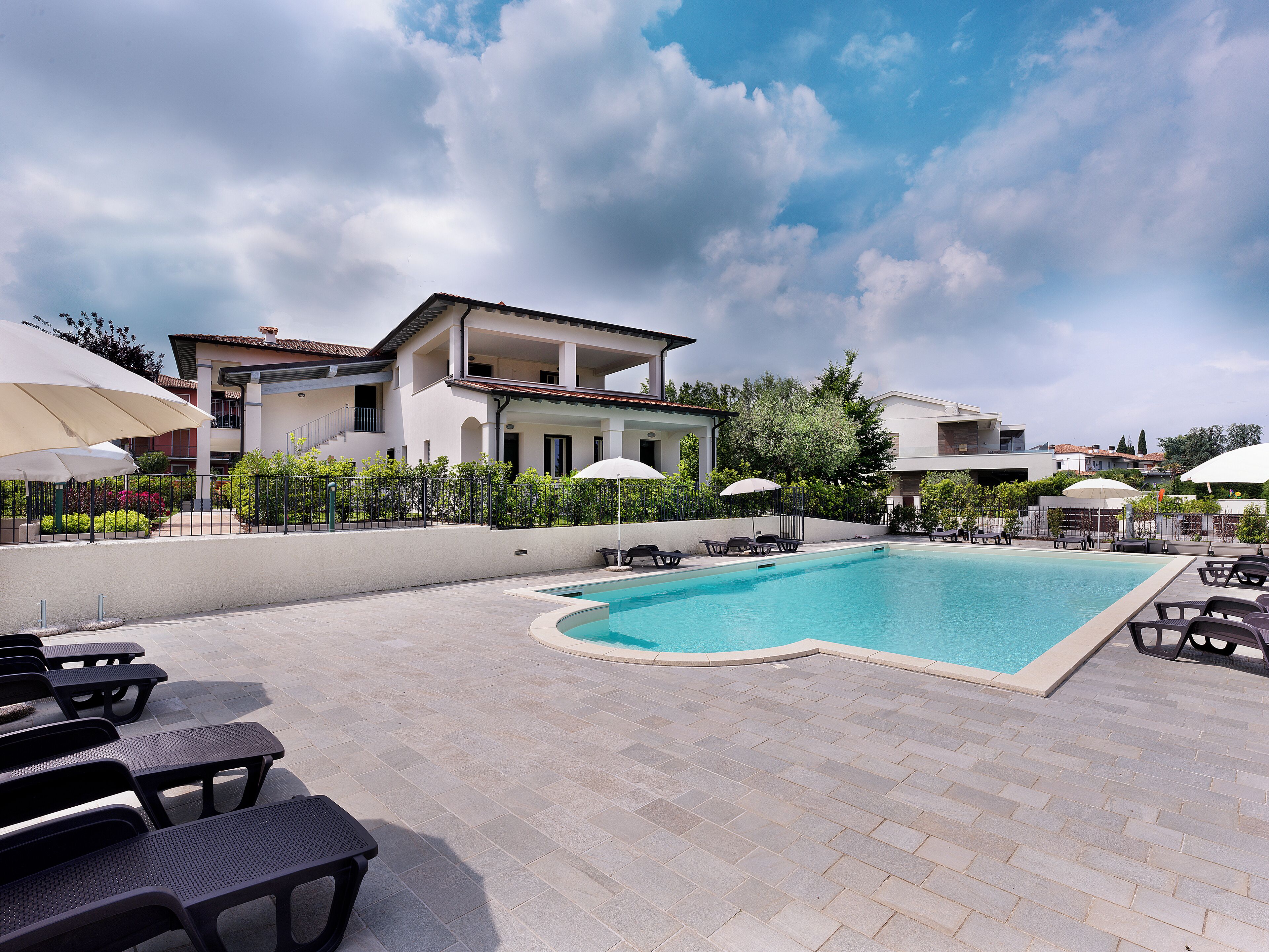 A swimming pool with lounge chairs and umbrellas, surrounded by a paved patio area.
