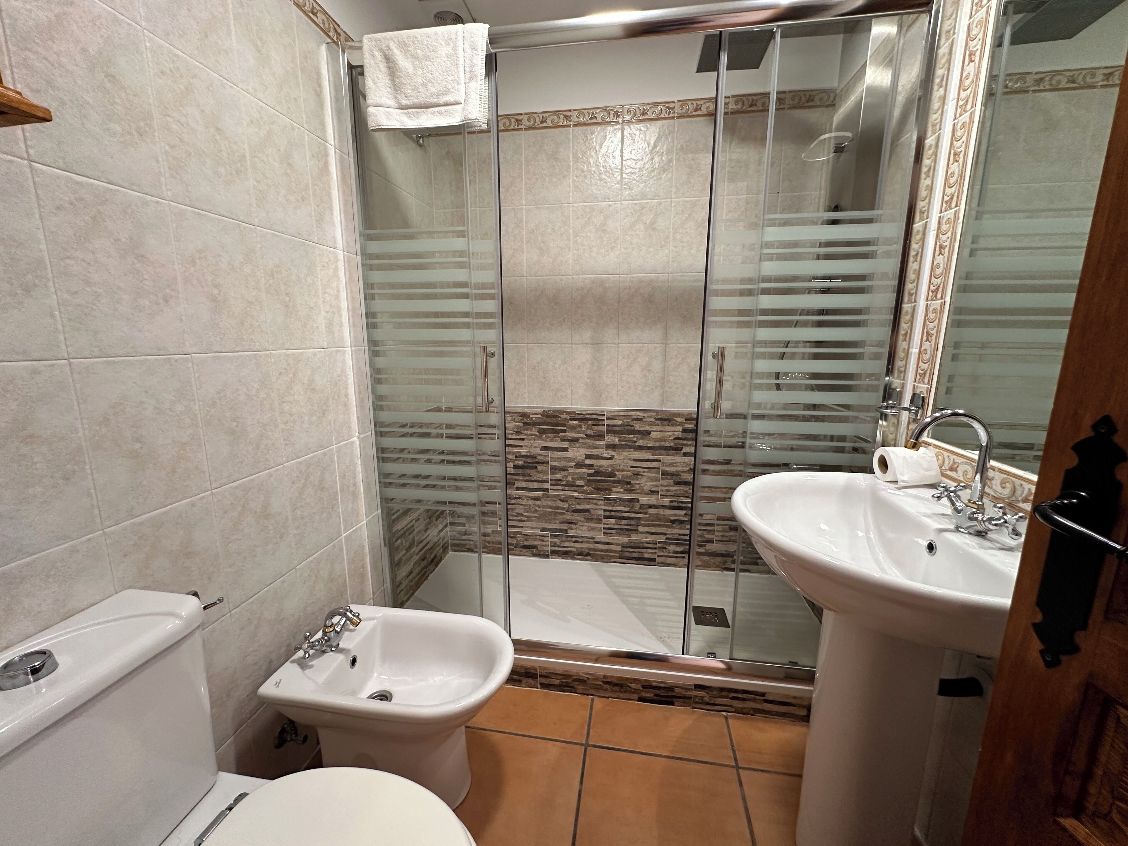 Un baño con inodoro, bidé, lavamanos y ducha con mampara de vidrio.