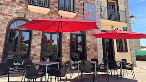 A stone building with a sign for Hotel Rural and Restaurante Posada La Fragua. There are outdoor tables and chairs with red umbrellas. - Hotel Posada La Fragua (Pinuecar-Gandullas)