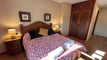 Un dormitorio con una cama de madera, dos mesitas de noche con lámparas, un armario con diseño calado y un ventilador de techo.