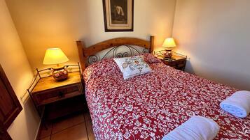 Una cama bien hecha con una colcha estampada con motivos florales, dos lámparas de noche, una mesita de noche de madera y un cuadro en la pared.
