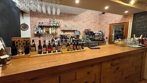 A bar area with a wooden counter, shelves of various liquor bottles, a coffee machine, and hanging glasses. - Hotel Posada La Fragua (Pinuecar-Gandullas)