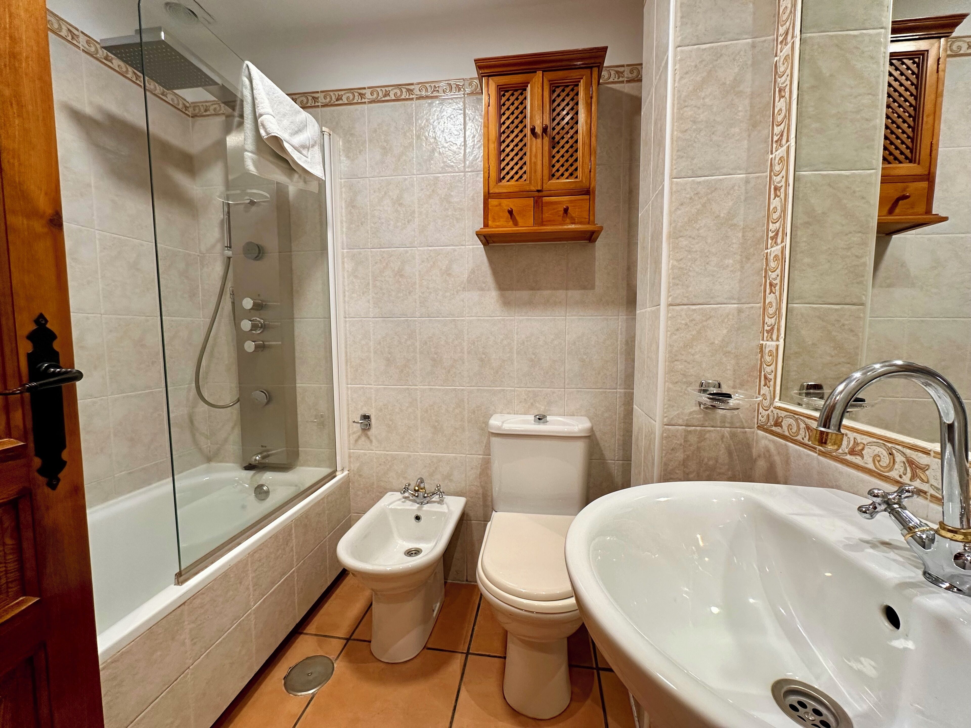 A bathroom with a glass-enclosed shower, a bidet, a toilet, and a sink with a large mirror.