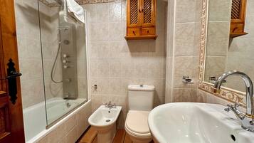 A bathroom with a glass-enclosed shower, a bidet, a toilet, and a sink with a large mirror.