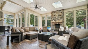 A sunroom with a stone fireplace, large windows, and comfortable seating.