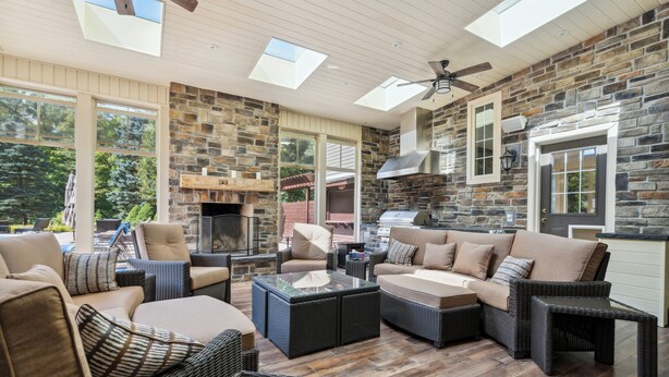 A spacious outdoor living area with stone walls, large windows, and comfortable seating.