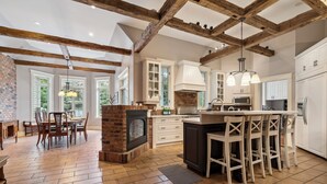 A spacious kitchen with a large island, wooden beams, and a brick fireplace.
