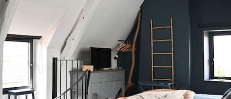 A bedroom with a sloped ceiling, a bed with a blue cover, a ladder, and a window.