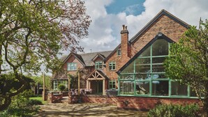 Ein traditionelles Backsteinhhaus mit großem Wintergarten, Garten und gepflasterter Auffahrt.