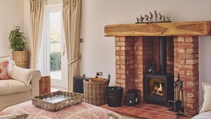 Ein gemütliches Wohnzimmer mit Kamin aus Backstein, Korbwannen und einer bequemen Couch.