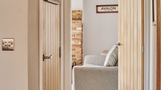 Ein Flur, der zu einem Schlafzimmer mit einem Bett, einer Ziegelwand und einem Schild mit der Aufschrift 'AVALON CATALINA ISLAND' führt.