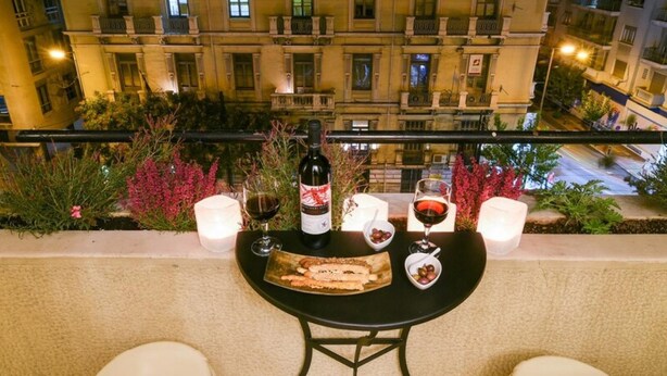 En balkon med et bord dækket til to personer, med vin, glas og en tallerken mad.
