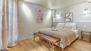 A bedroom with a bed, a bench, a bedside table, and a wall-mounted light.