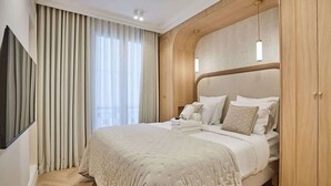 A hotel room with a large bed, a TV mounted on the wall, and a wooden wardrobe. - Apartment in the Marais with Air-conditioned (Paris)