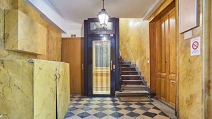 A hallway with a checkered floor, a staircase, and a door with a light fixture above it. - Apartment in the Marais with Air-conditioned (Paris)