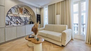 A modern living room with a beige sofa, a marble wall, and a large window with curtains. - Apartment in the Marais with Air-conditioned (Paris)