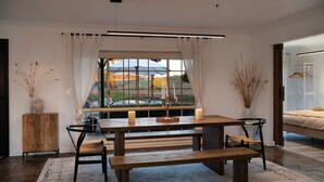 A dining area with a wooden table, benches, and a view of a natural landscape through a large window. - Sunset Retreat-amaxing views over Mt Franklin (Franklinford)